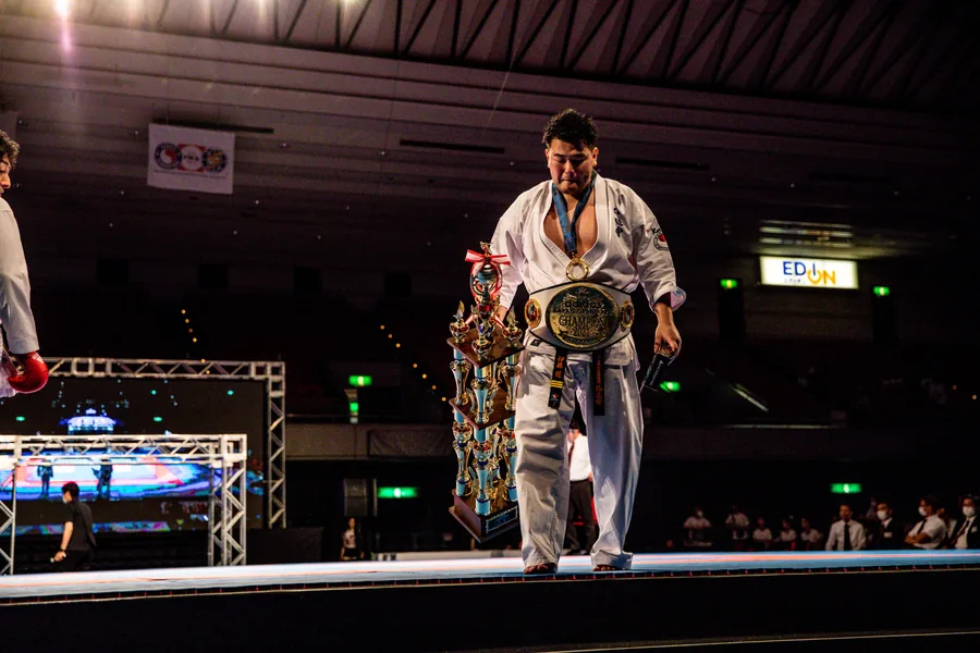 A champion holds a trophy while wearing a title belt at the 2021 national tournament awards.